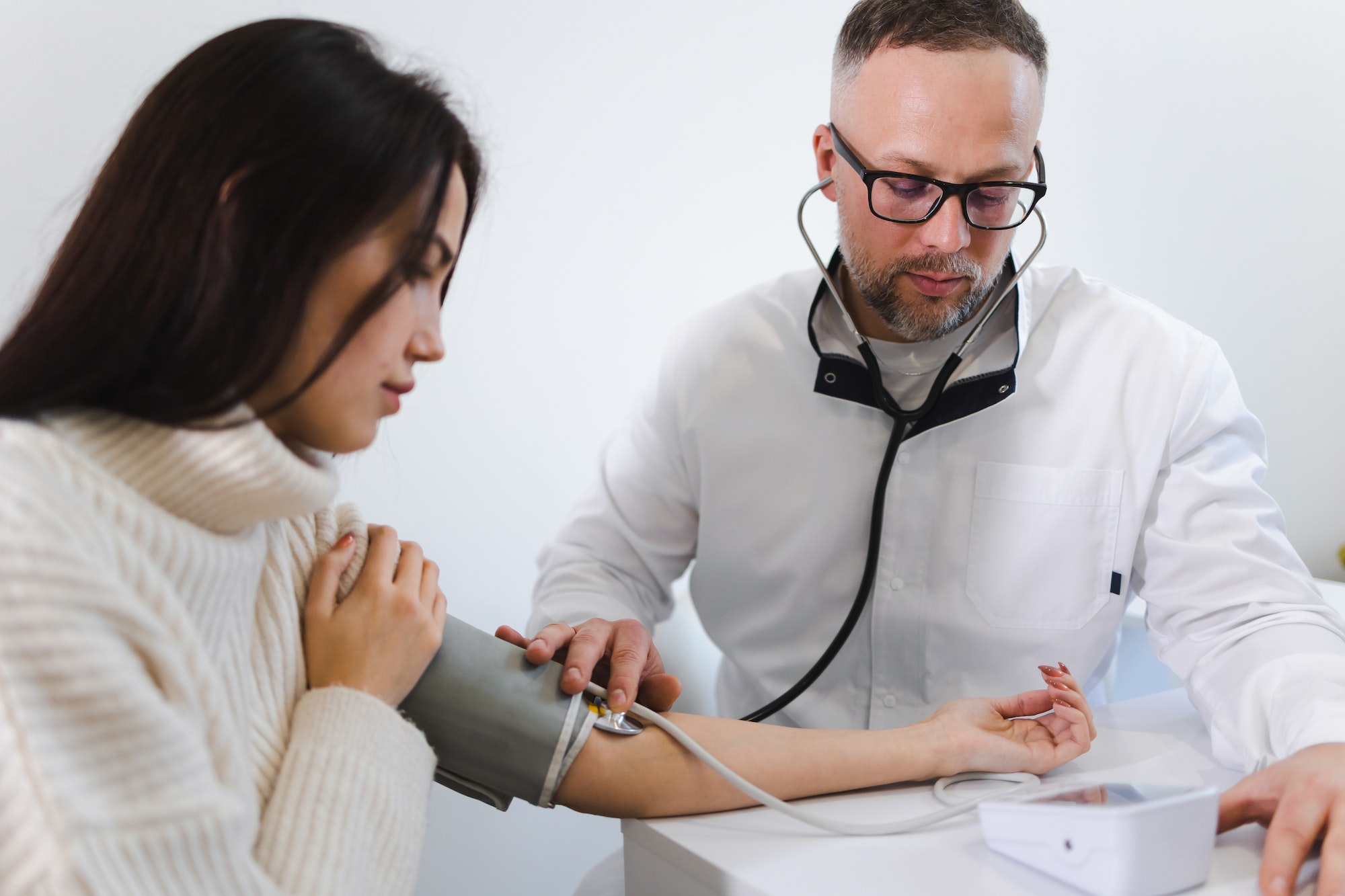 Male doctor at the medical examination measures the blood pressure of a woman patient.